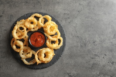 Delicious onion rings and sauce on gray background, top view. Space for text