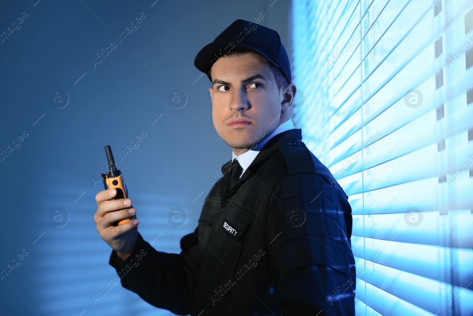 Photo of Professional security guard with portable radio set near window in dark room