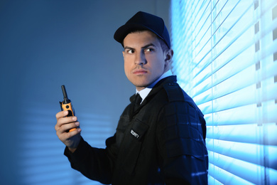 Professional security guard with portable radio set near window in dark room