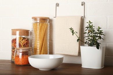 Beautiful plant and different products on wooden table near white brick wall in kitchen