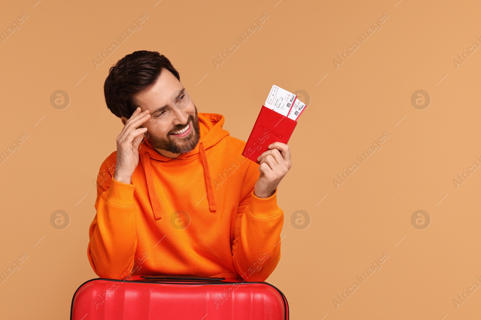 Photo of Smiling man with passport, suitcase and tickets on beige background. Space for text