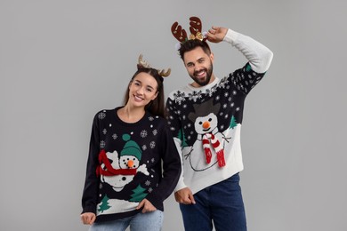 Photo of Happy young couple in Christmas sweaters and reindeer headbands on grey background