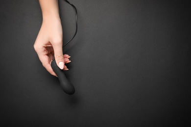 Photo of Young woman holding little vibrator and charging cable on black background, top view with space for text. Sex toy