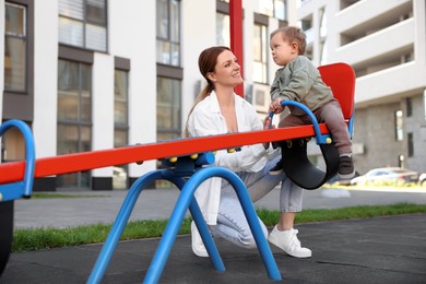 Photo of Happy nanny and cute little boy on seesaw outdoors