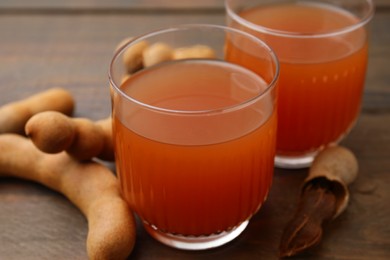 Photo of Tamarind juice and fresh fruits on wooden table, closeup