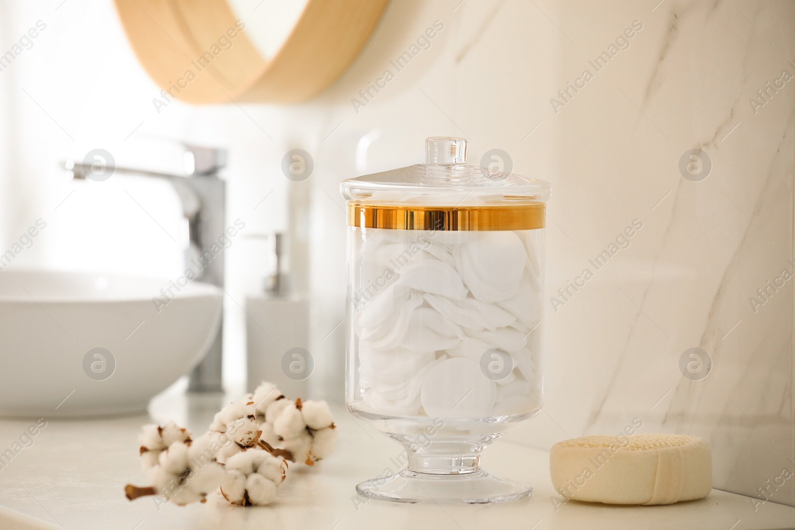 Photo of Jar with cotton pads and flowers on countertop in bathroom