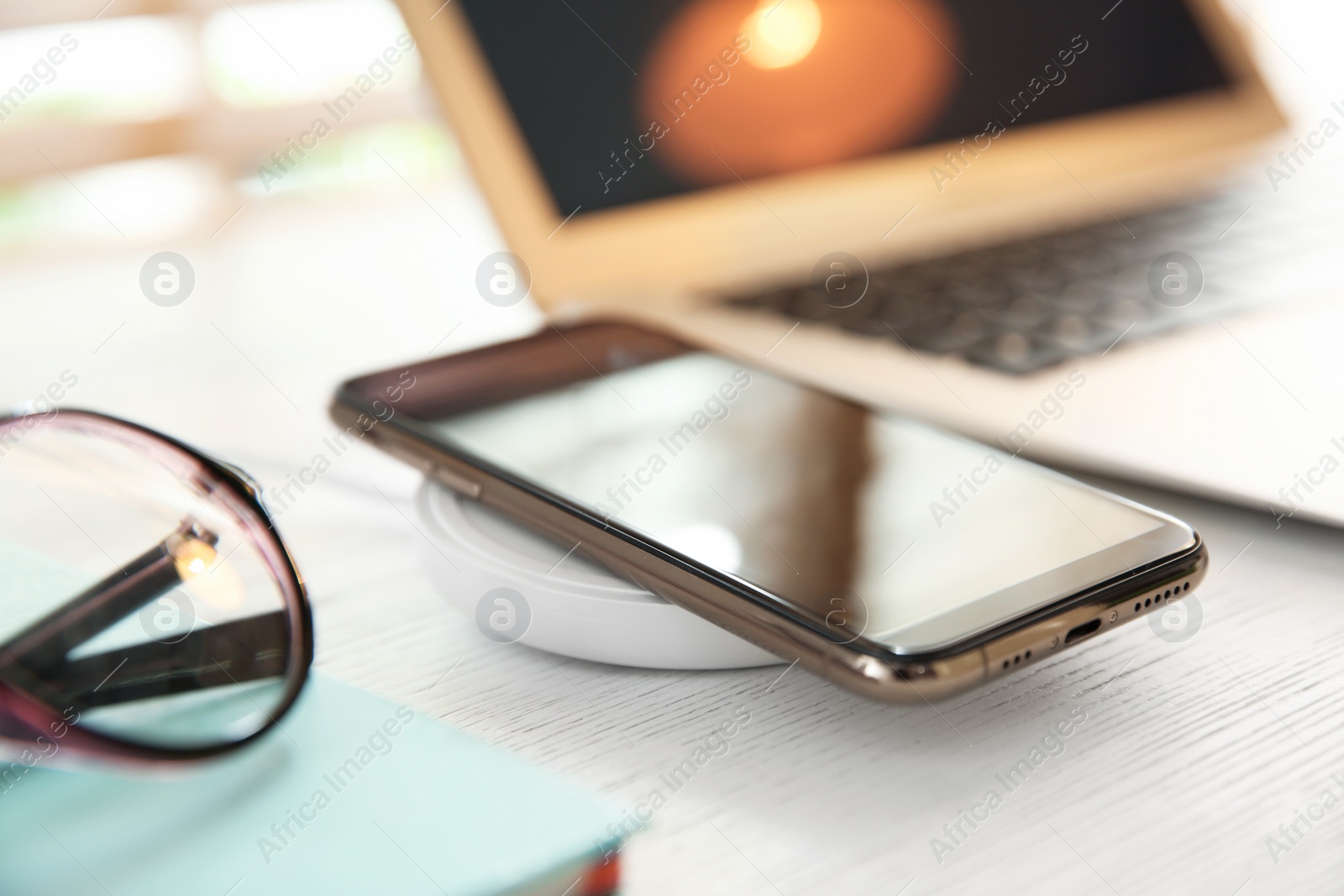 Photo of Mobile phone with wireless charger on white wooden table. Modern workplace accessory