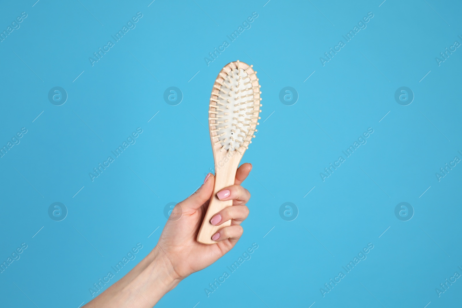 Photo of Woman holding wooden hair brush against blue background, closeup. Space for text