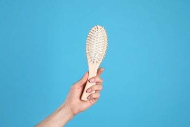 Woman holding wooden hair brush against blue background, closeup. Space for text