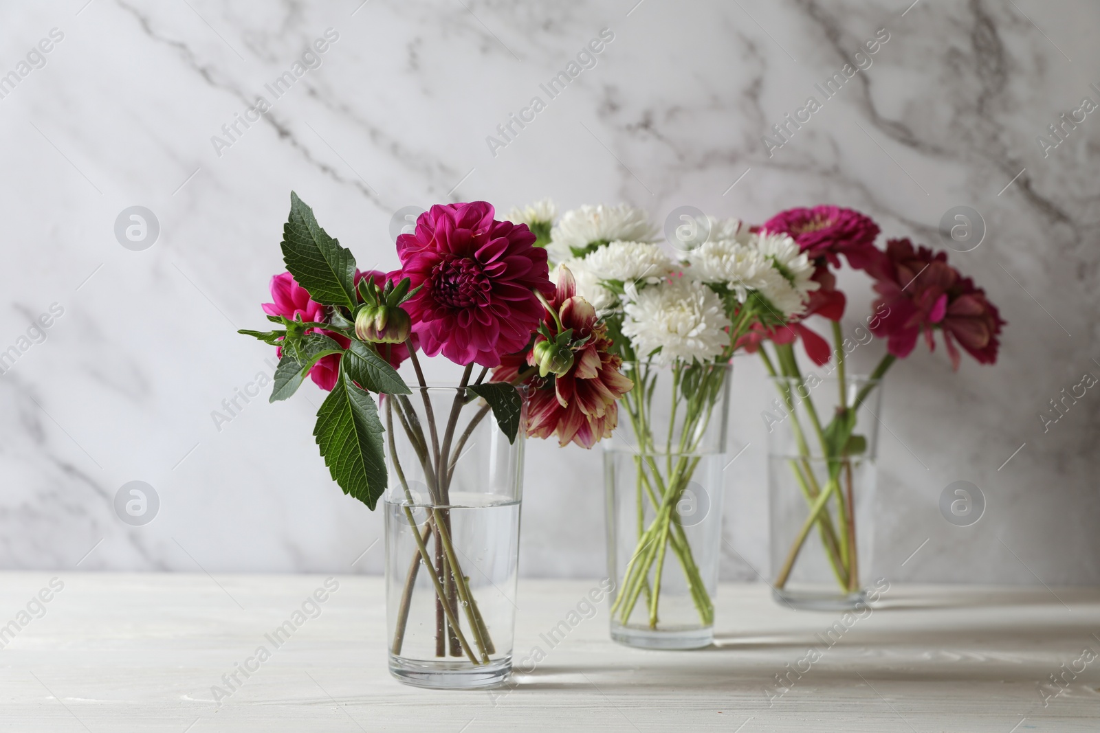 Photo of Bouquet of beautiful wild flowers and leaves in vases on white wooden table against marble background