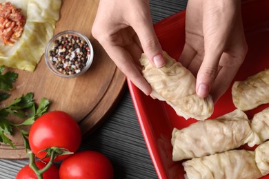 Woman putting uncooked stuffed cabbage roll into baking dish at black table, top view