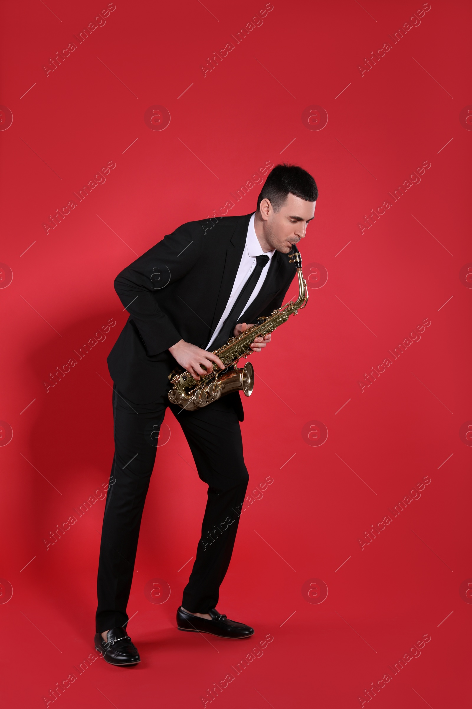 Photo of Young man in elegant suit playing saxophone on red background