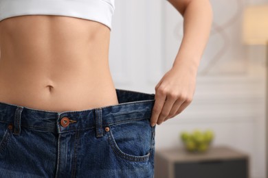 Photo of Slim woman wearing big jeans in room, closeup. Weight loss