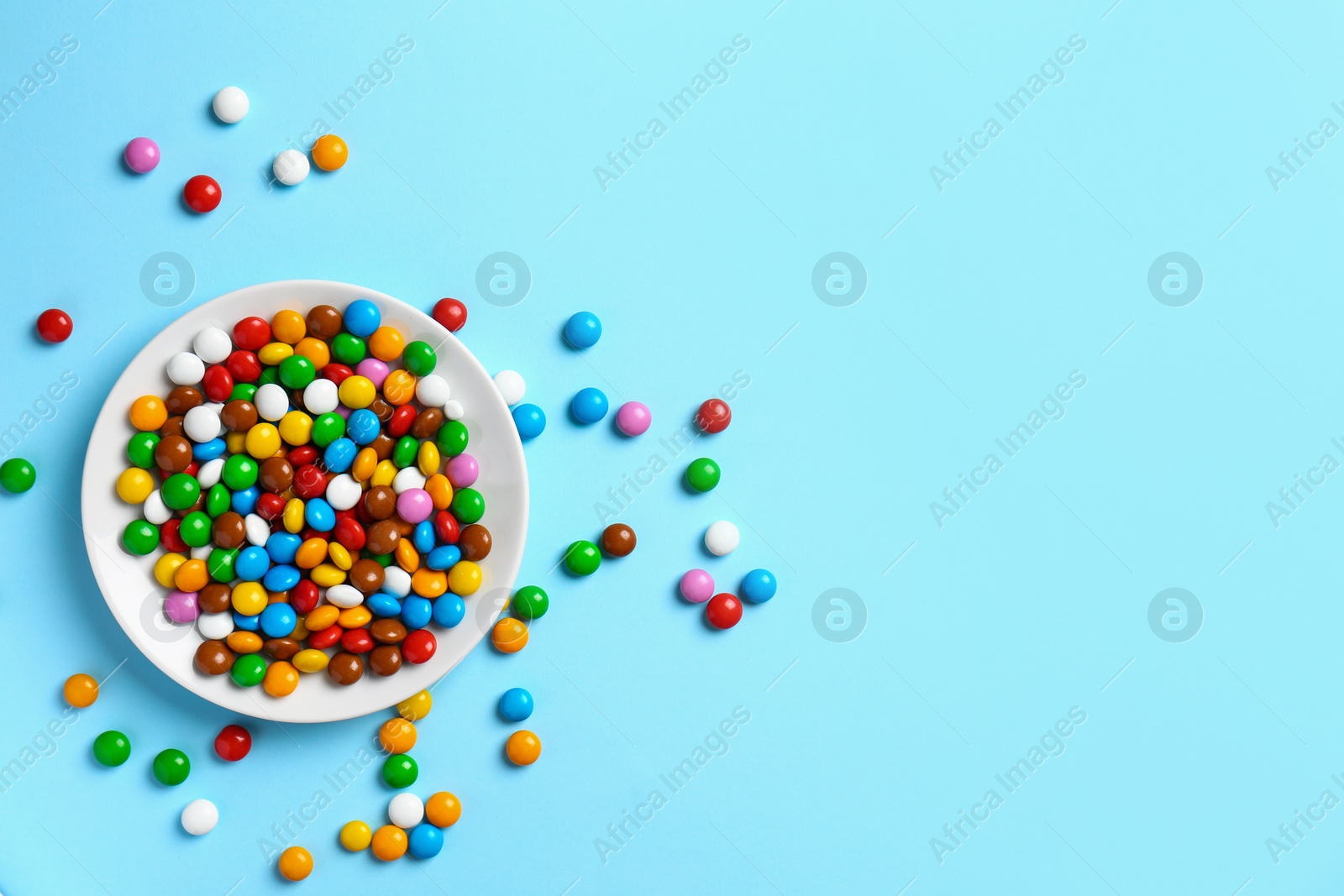 Photo of Delicious bright glazed candies on light blue background, top view. Space for text