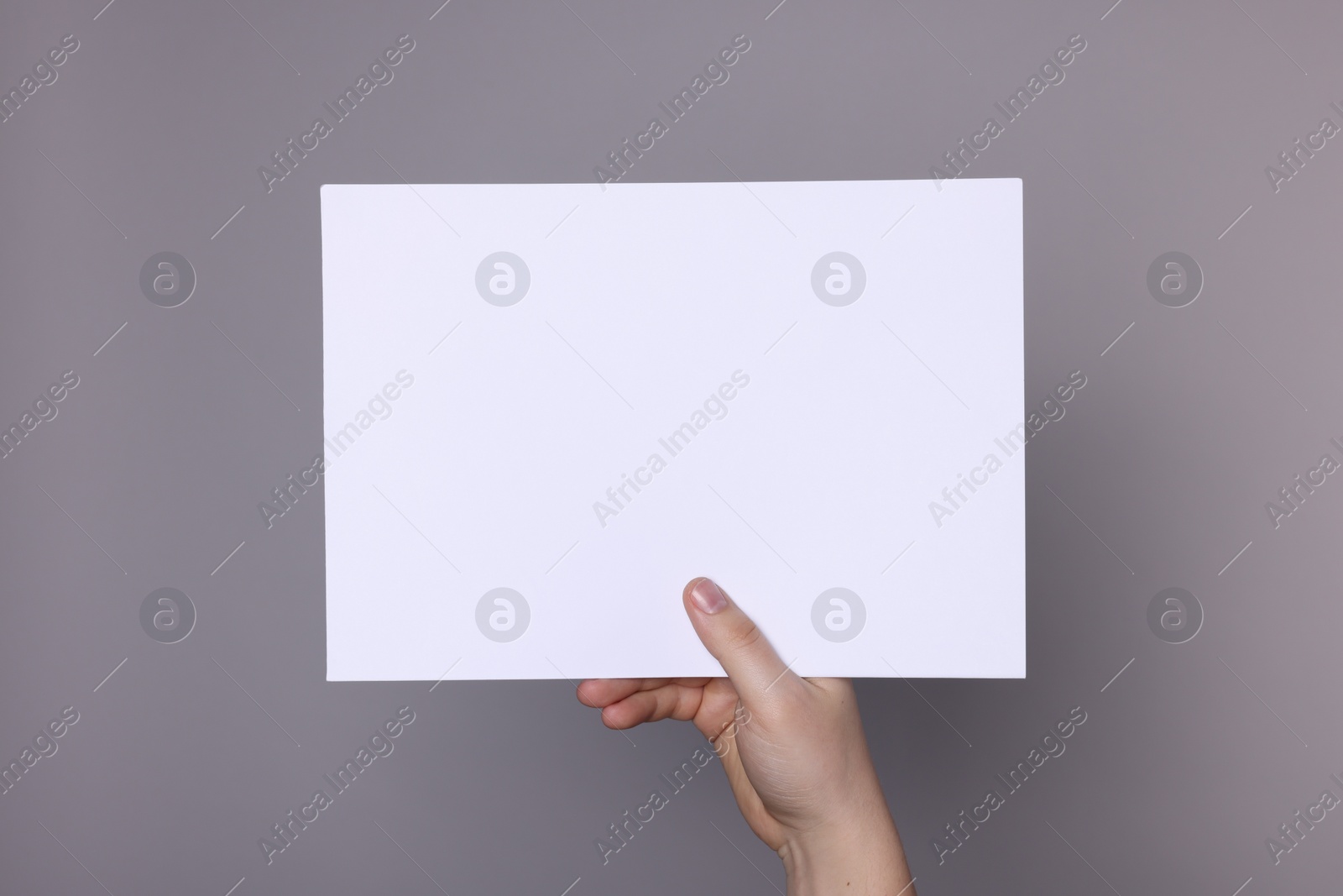 Photo of Woman holding sheet of paper on grey background, closeup. Mockup for design