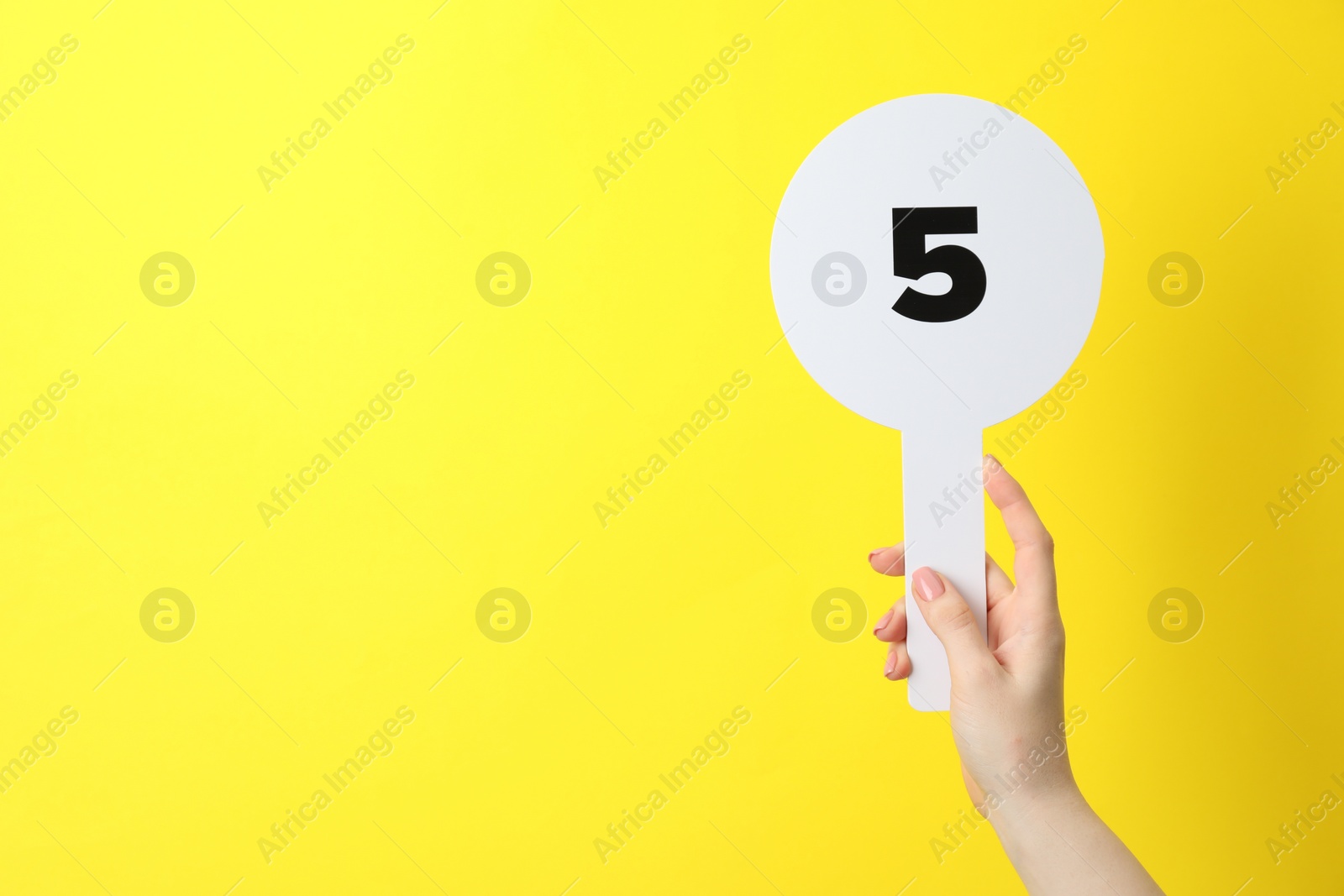 Photo of Woman holding auction paddle with number 5 on yellow background, closeup. Space for text