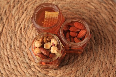 Photo of Jars with different nuts and honey on wicker mat, above view