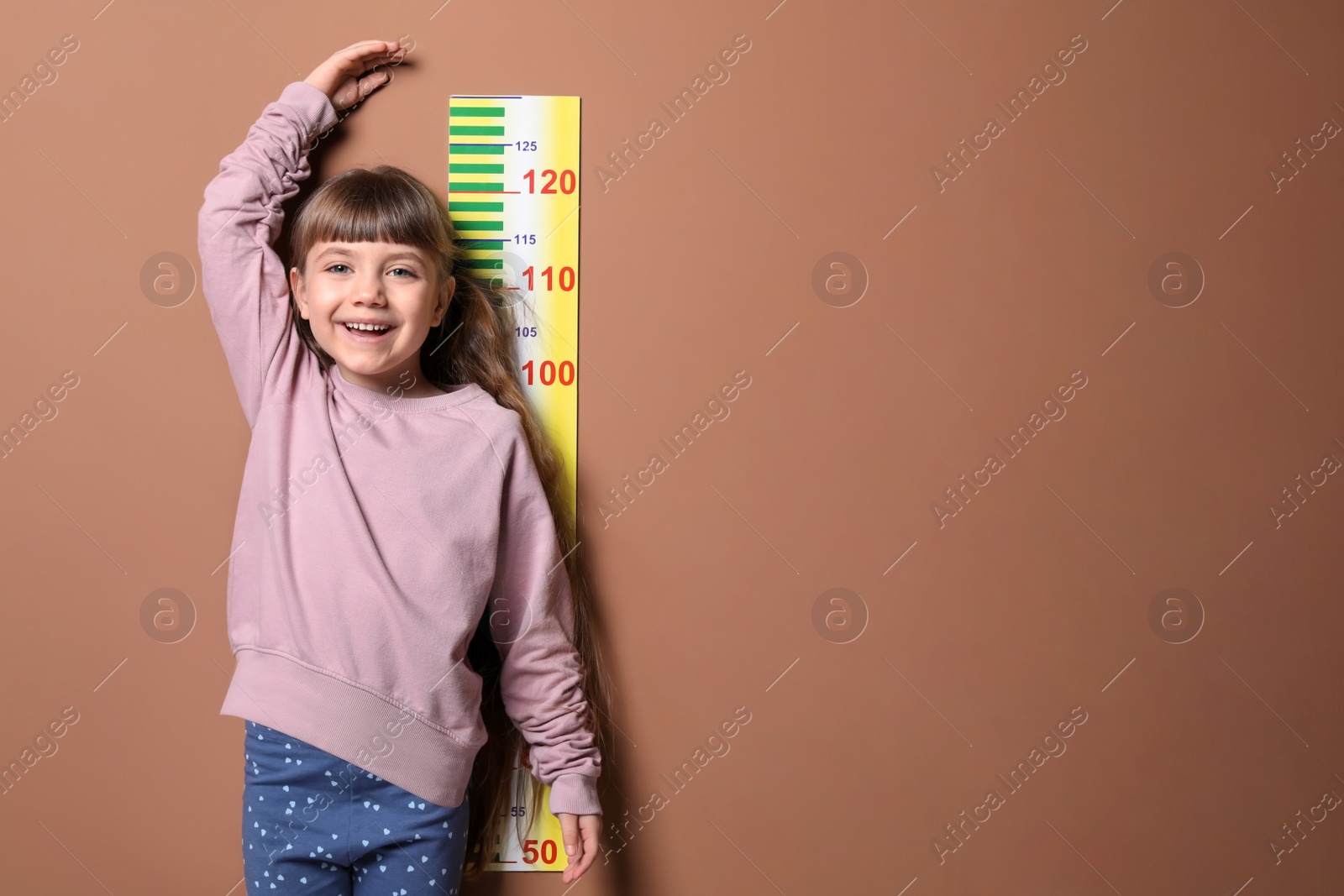 Photo of Little girl measuring her height on color background