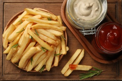 Photo of Delicious french fries served with sauces on wooden board, flat lay