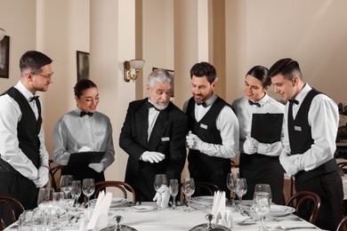 Photo of Senior man wearing formal suit teaching trainees in restaurant. Professional butler courses