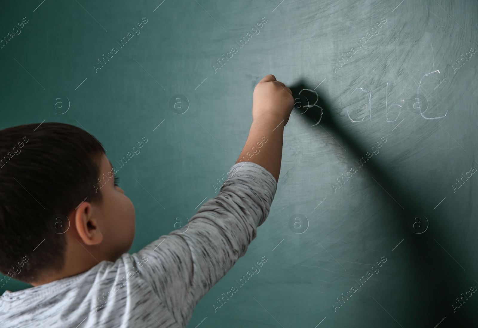 Photo of Little child writing math sum on chalkboard