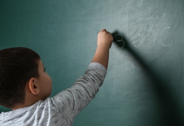 Little child writing math sum on chalkboard