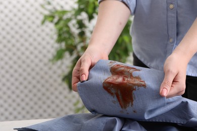 Photo of Woman showing stain from sauce on shirt against blurred background, closeup. Space for text