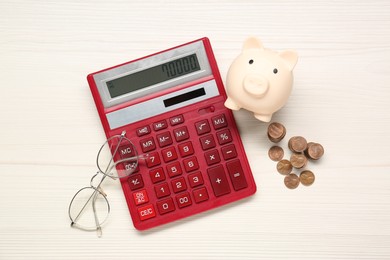 Calculator, piggy bank, coins and glasses on white wooden table, flat lay