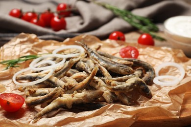 Delicious fried anchovies with onion rings and tomatoes served on table, closeup