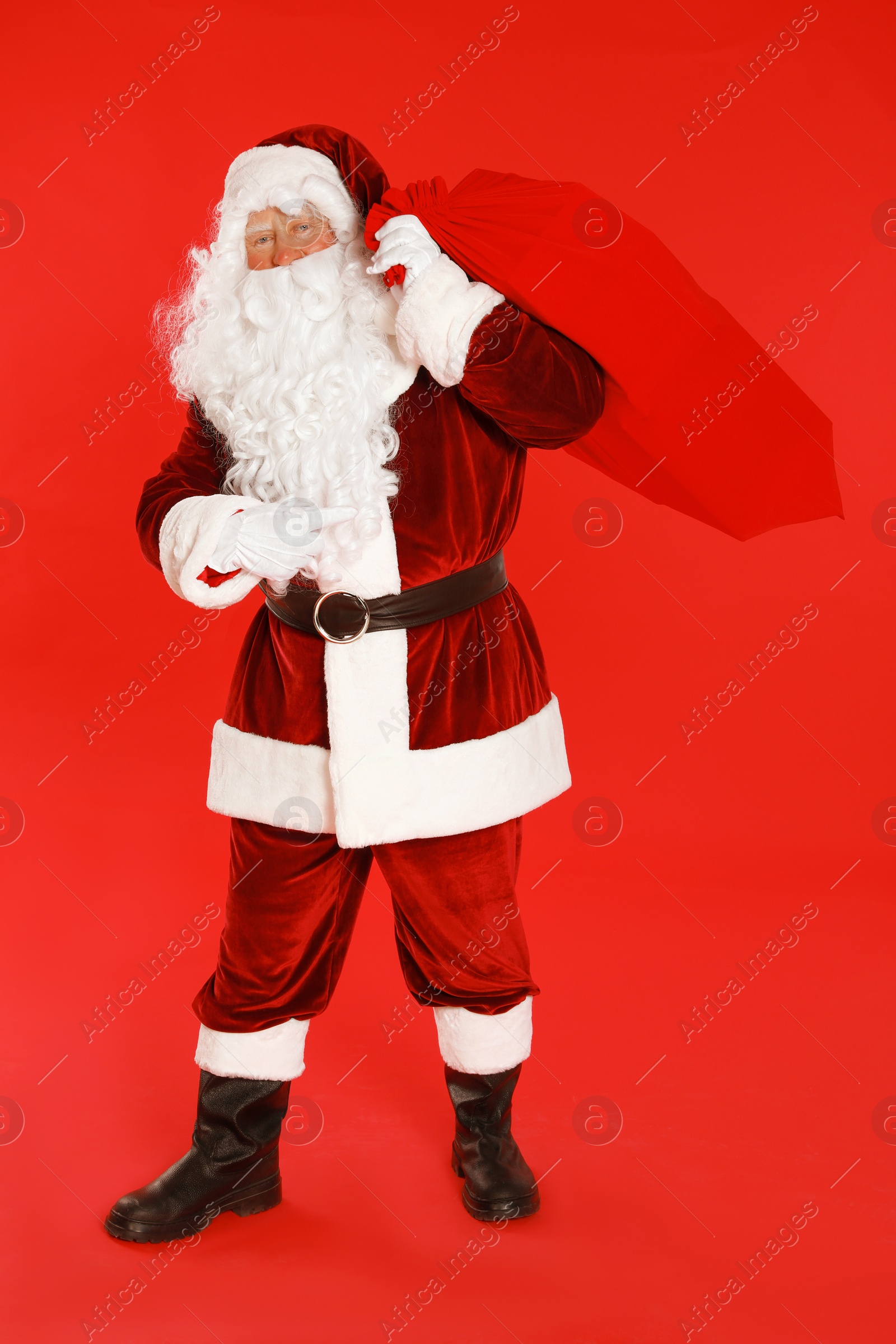 Photo of Authentic Santa Claus with bag full of gifts on red background