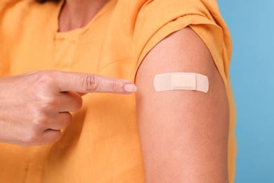 Photo of Woman pointing at adhesive bandage after vaccination on light blue background, closeup