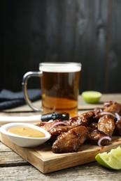 Photo of Tasty roasted chicken wings served with beer on wooden table, closeup