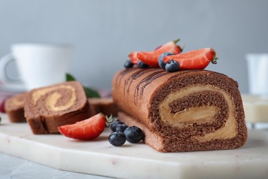 Tasty chocolate cake roll with cream and berries on board, closeup