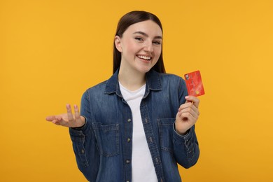 Happy woman with credit card on orange background