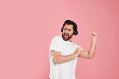 Photo of Emotional man listening music with headphones on pink background. Space for text