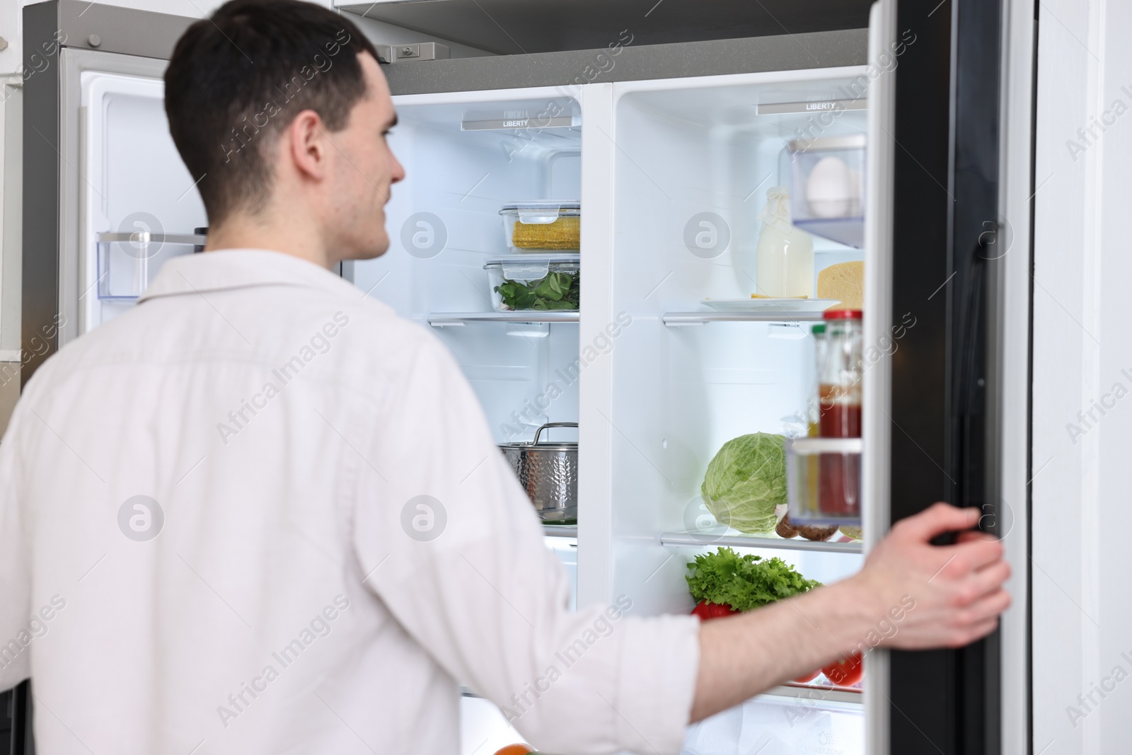 Photo of Man near refrigerator in kitchen at home, back view