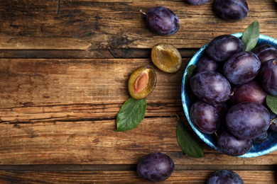 Photo of Delicious ripe plums on wooden table, flat lay. Space for text