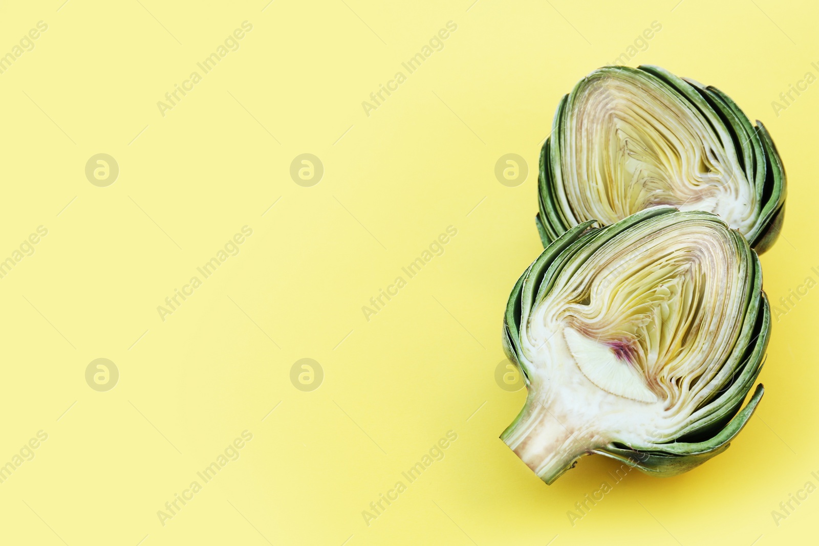 Photo of Halves of fresh raw artichoke on pale yellow background. Space for text