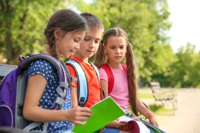 Photo of Cute little children with backpacks and notebooks outdoors. Elementary school