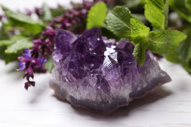 Photo of Amethyst gemstone and healing herbs on white wooden table, closeup
