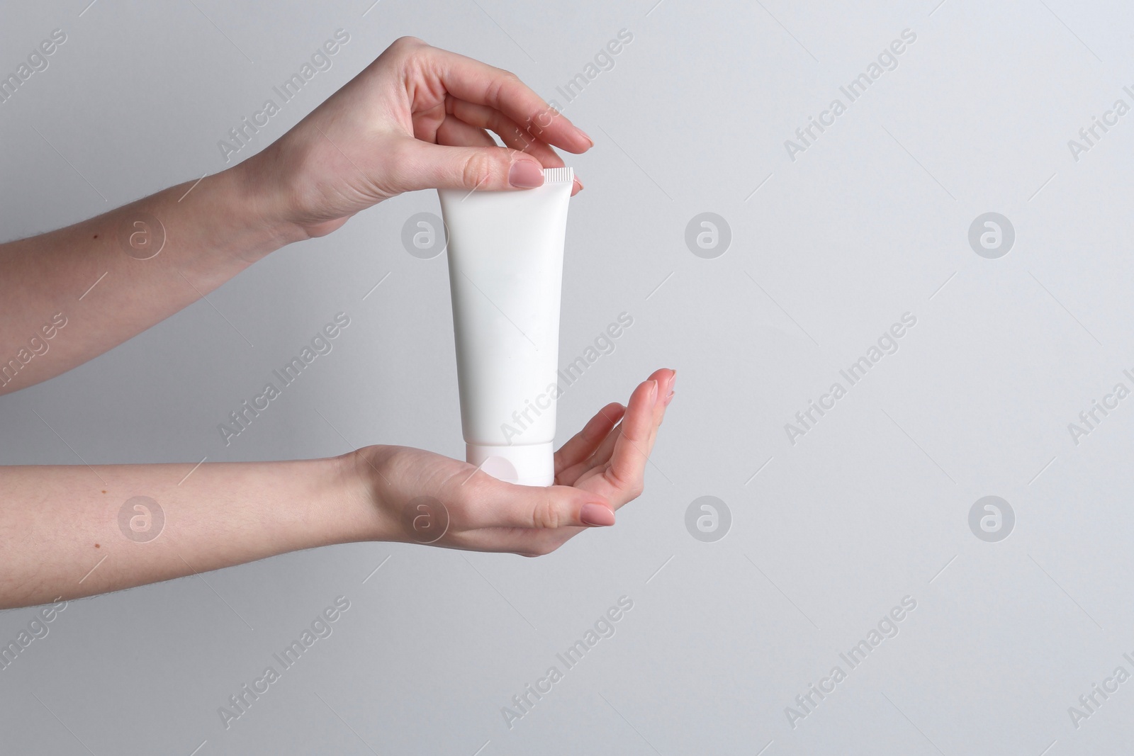 Photo of Woman holding tube of cream on grey background, closeup. Space for text