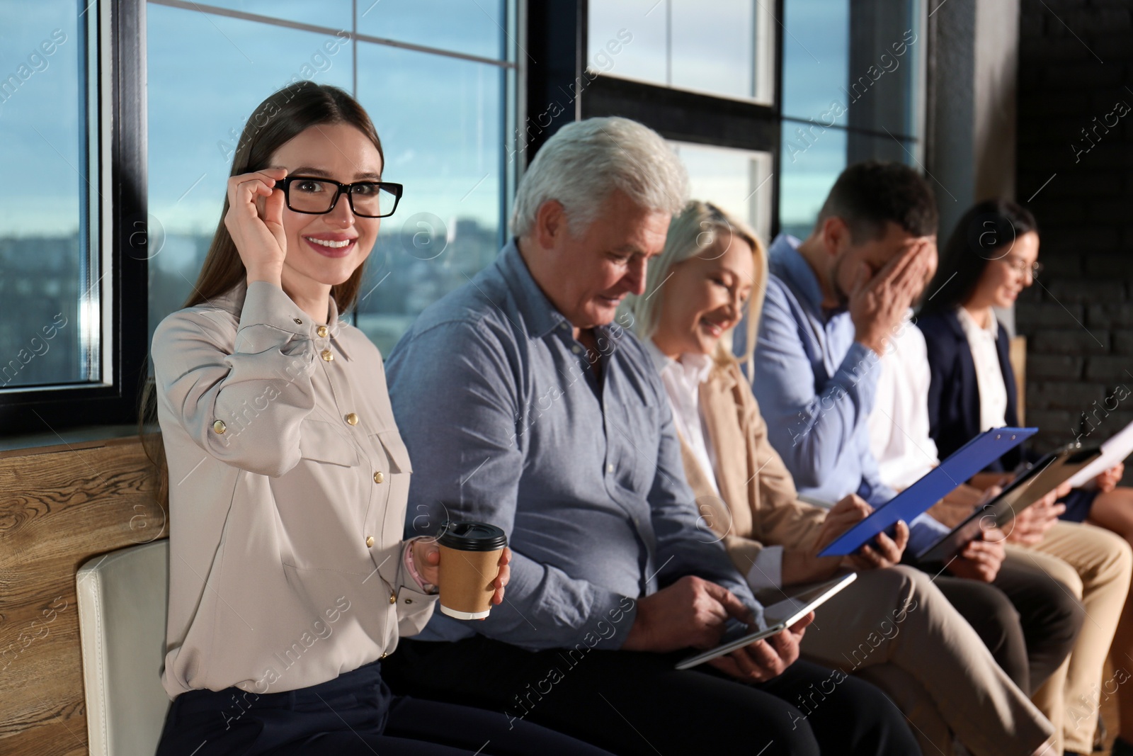 Photo of Young woman with eyeglasses and cup of coffee waiting for job interview in office hall