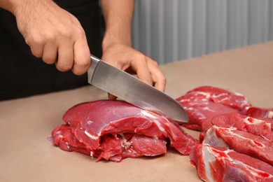 Butcher cutting fresh raw meat on counter in shop, closeup