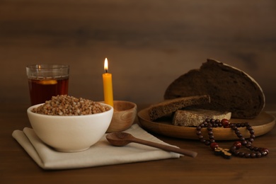 Photo of Buckwheat porridge, spoon, rosary beads, bread and candle on wooden table. Lent season