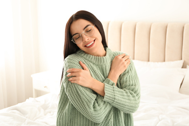 Photo of Young woman wearing warm sweater on bed at home. Winter season