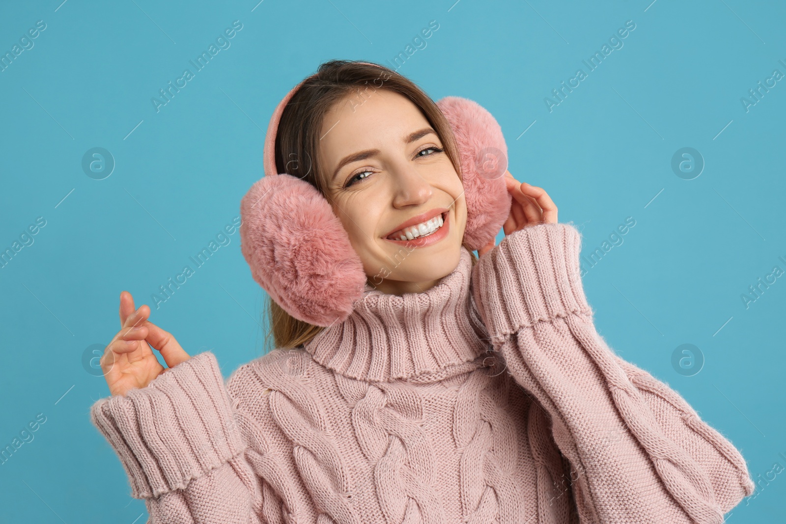 Photo of Happy woman wearing warm earmuffs on light blue background