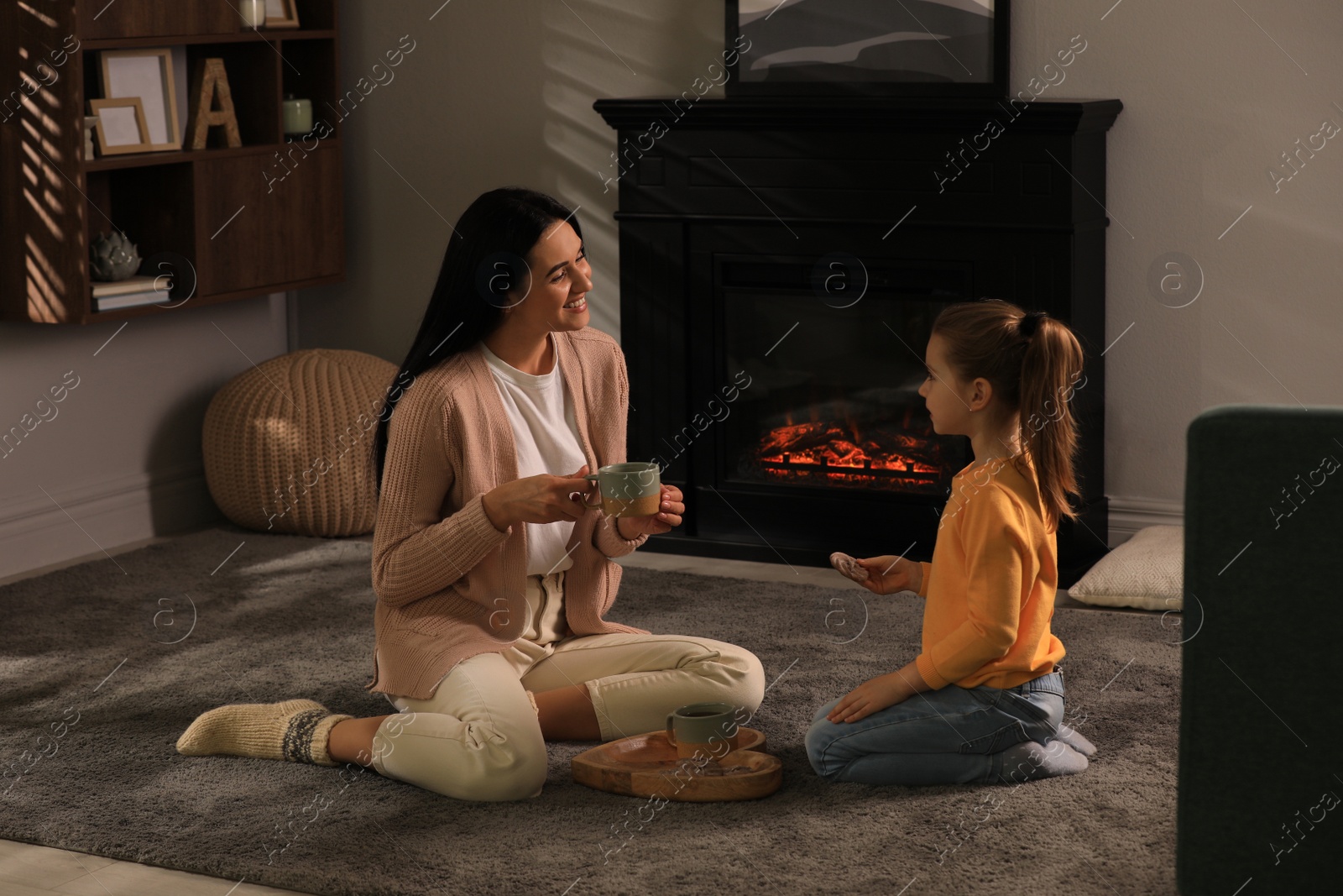 Photo of Happy mother and daughter spending time together on floor near fireplace at home