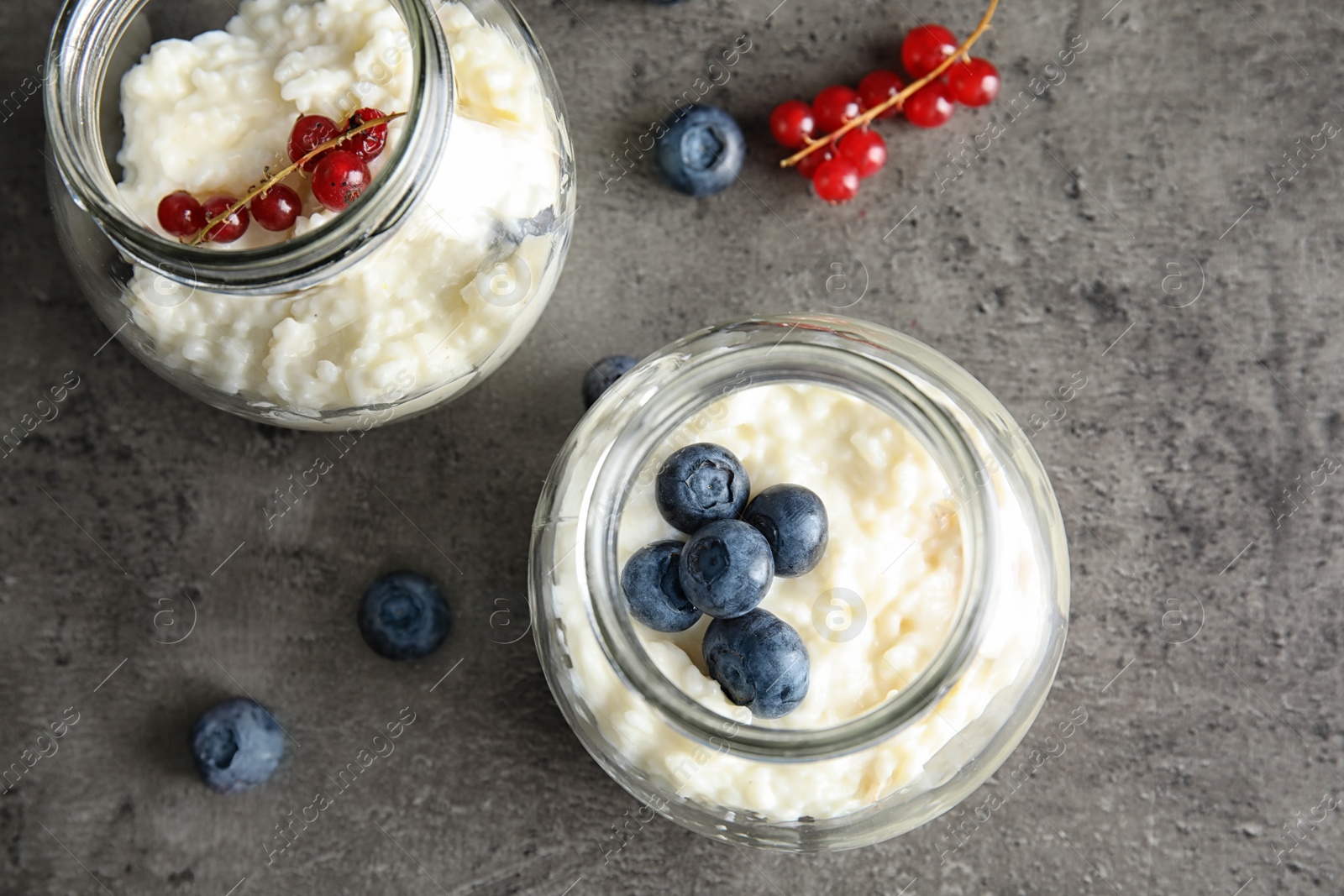 Photo of Creamy rice pudding with red currant and blueberries in jars on grey background