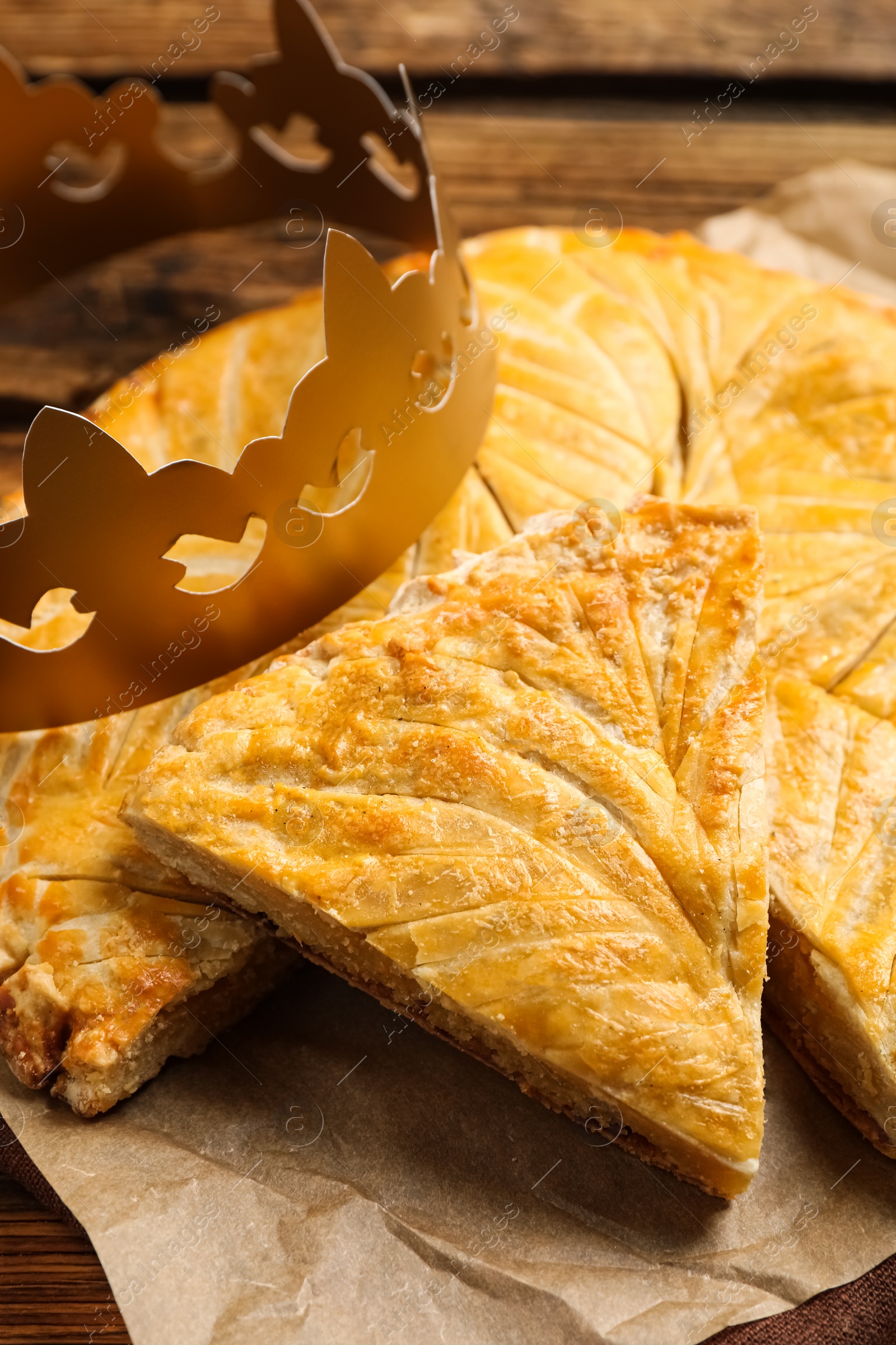 Photo of Traditional galette des Rois with paper crown on wooden table, closeup