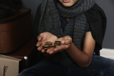 Photo of Poor homeless boy with coins begging near dark wall, focus on hands